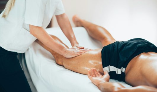 Leg massage. Physical therapyst massaging leg of young male athe